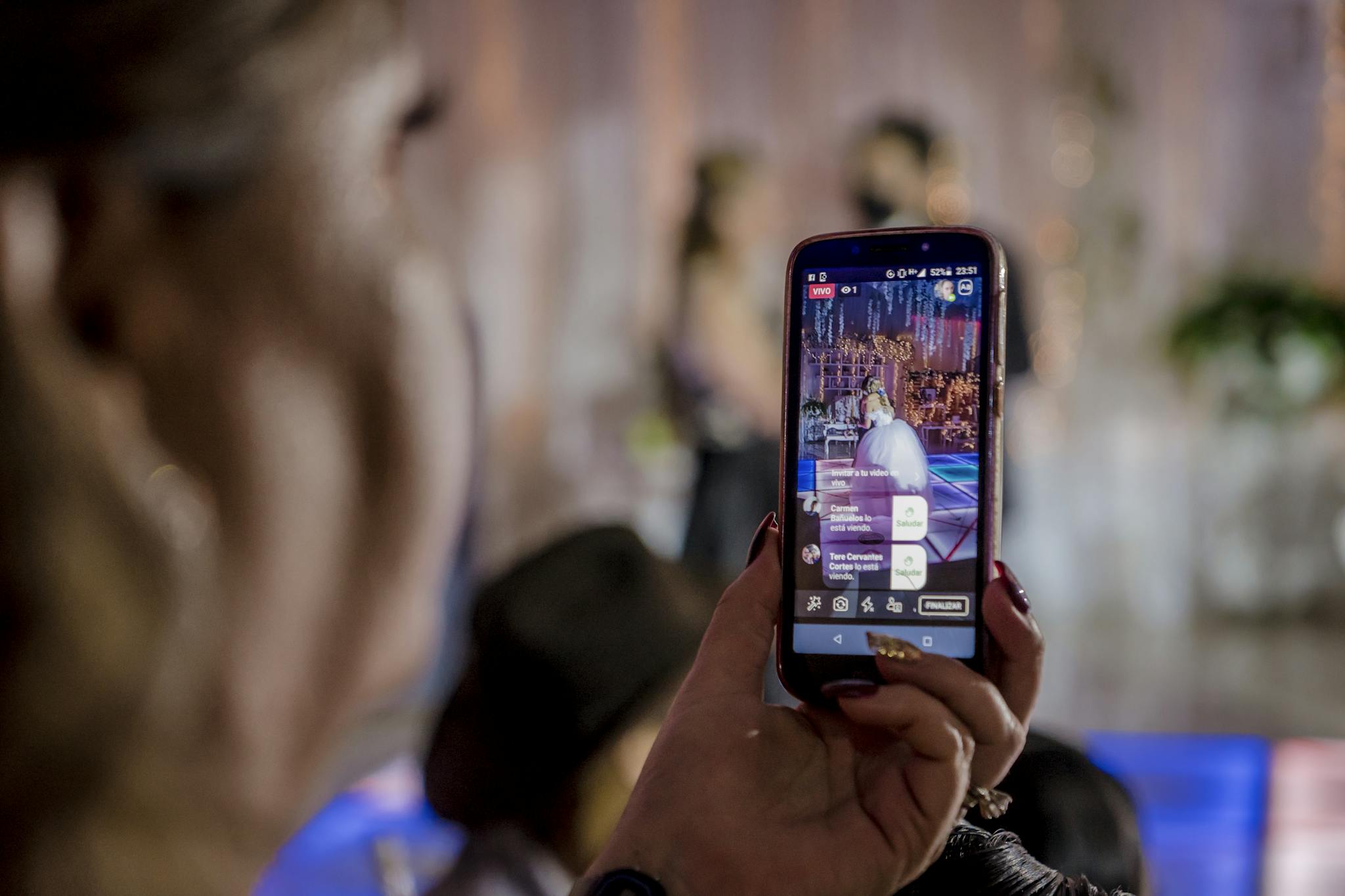 A woman captures a live event video using a smartphone at a lively indoor gathering.